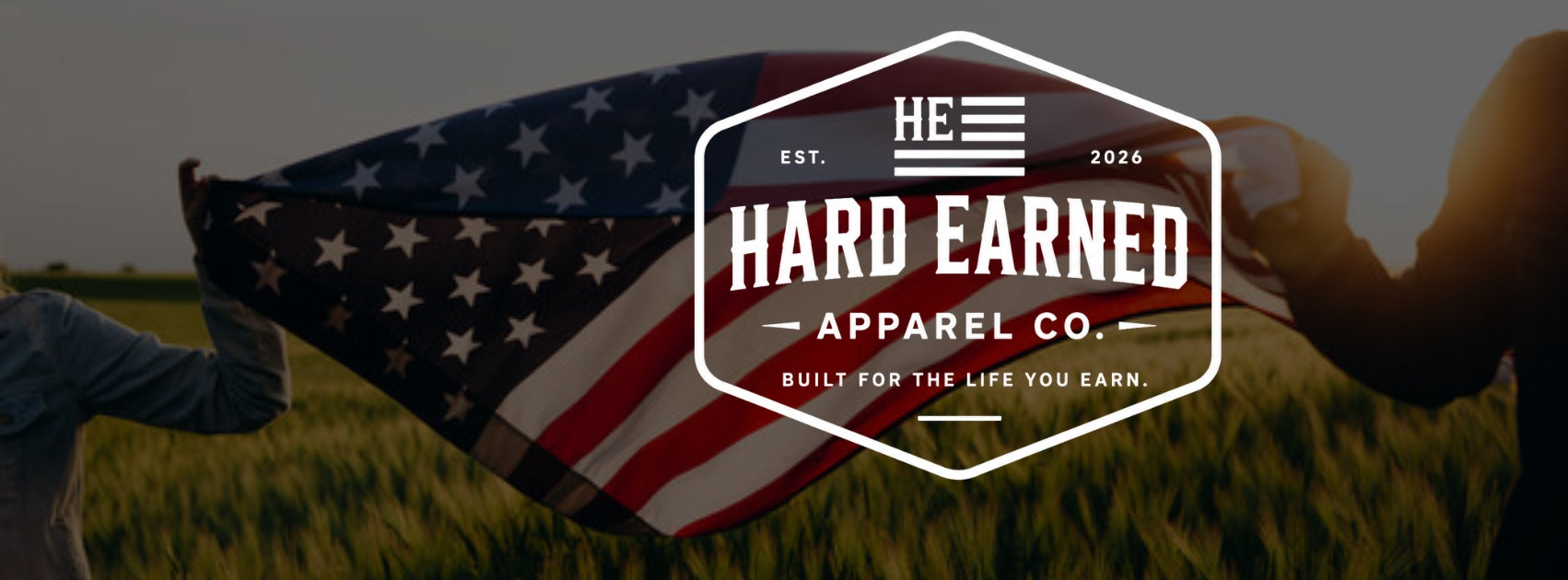 American flag held by two people with 'The Hard Earned Apparel Co.' logo overlay